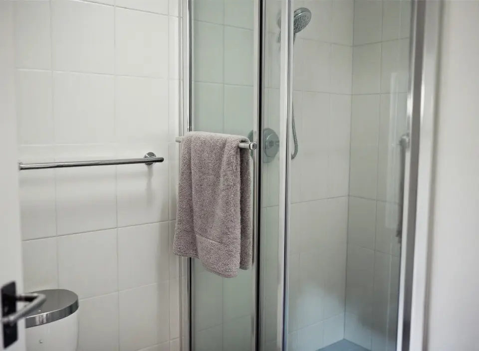 Een kleine witte badkamer met een douchecabine, een douchekop aan een glijstang en een handdoek